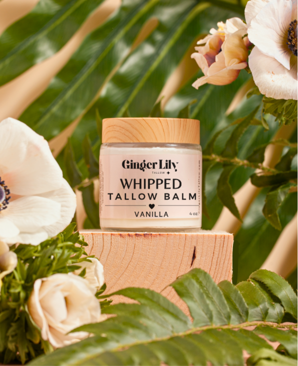 Jar of Ginger Lily Whipped Tallow Balm on a wooden block with flowers and greenery in the background