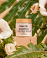 Jar of Ginger Lily Whipped Tallow Balm on a wooden block with flowers and greenery in the background